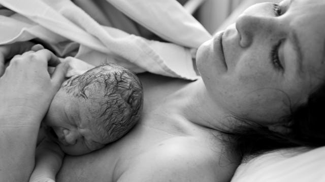 A mother lying down in a hospital bed with her newborn baby on her chest immediately after birth in ...