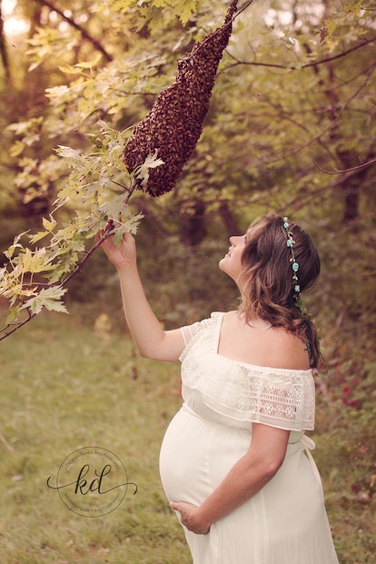 A pregnant woman in a white dress is touch a tree branch during a sunny day