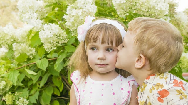 A 'kissy' blonde boy kissing a girl on the cheek even though his affection is unwanted in this situa...