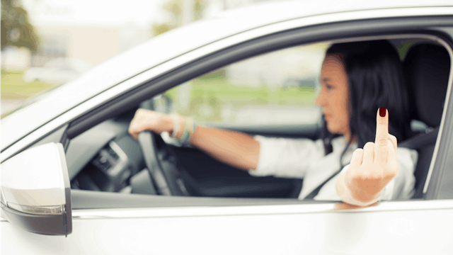 A woman driving her car, pointing a middle finger through the window