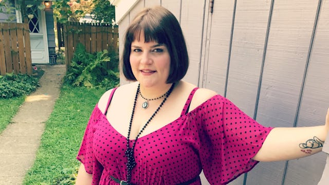 A woman dressed in a pink dress with black dots standing in the backyard
