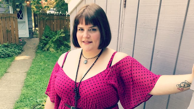 A woman dressed in a pink dress with black dots standing in the backyard