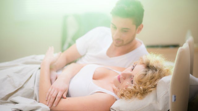 A woman in a white tank top and a man next to her in a white T-shirt lying in bed
