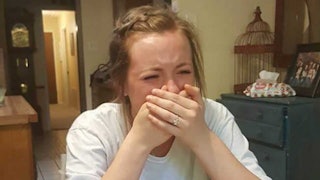 A young woman crying with her hands over her mouth while sitting at the dining table