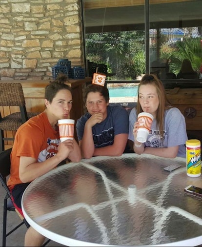 A woman with her two brothers at a table outdoors drinking sodas 