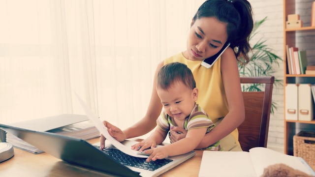 A mom talking on the phone and doing work while holding her baby.