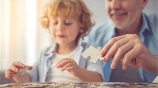 Grandparent playing puzzles with his grandchild in a sunny room while both of them are wearing blue ...