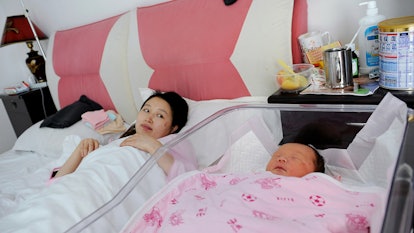 A mother in China lying in a bed next to her baby's crib during her zuo yuezi period.