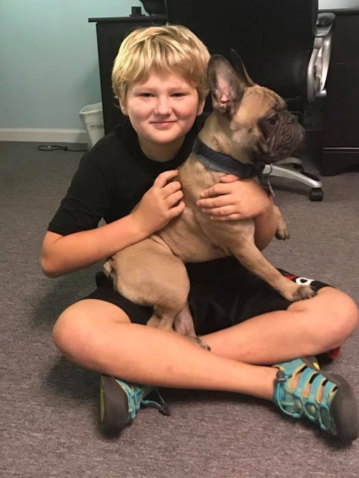 Natania Barron's autistic son sitting on the floor, holding a dog 