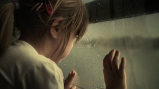 A little girl looking from the window with her hands on the window glass who suffers from emotional ...