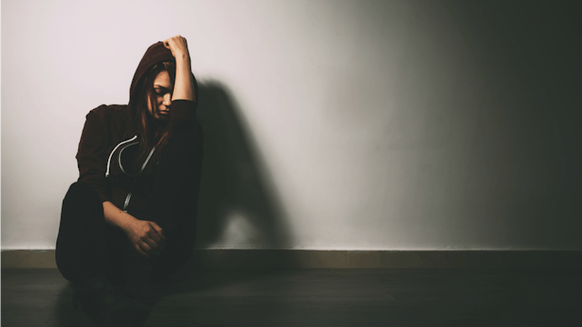 A girl in black clothes sitting in the corner with her head down who shares the story of her rape