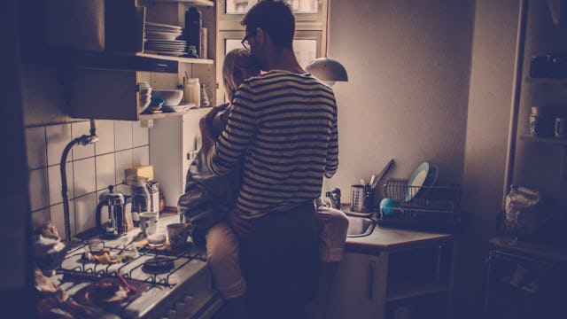 A woman sitting on a kitchen counter and a man in a black and white striped sweater hugging her 
