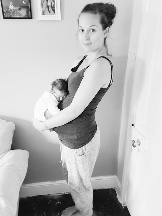Vicki Cockerill in a black tank top and sweatpants holding her baby next to a door in black and whit...