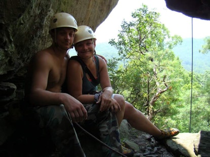 Couple posing at the edge of a rock while wearing helmets 
