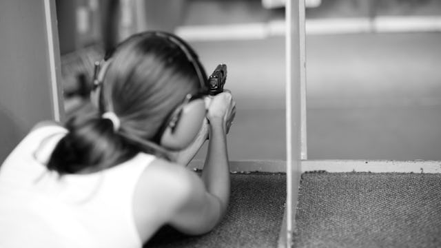 A woman in a white top pointing a gun at the gun range