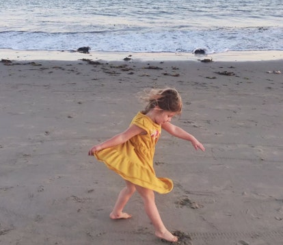 A girl in a yellow dress walking on a beach