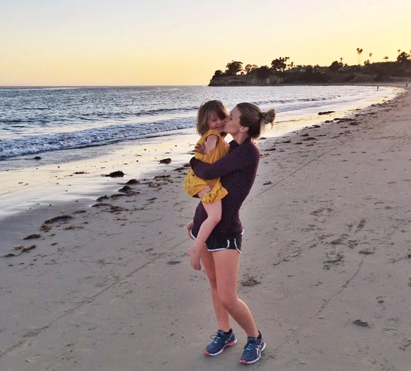 A woman kissing her daughter at the beach. 