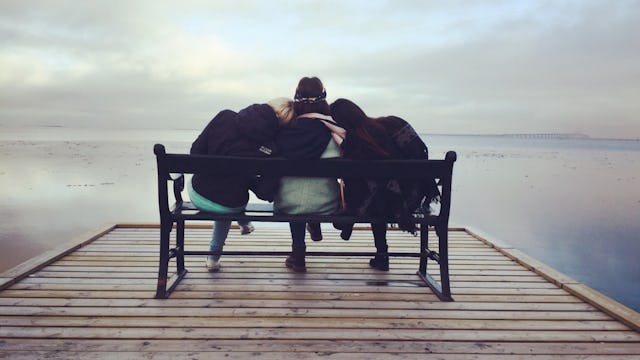 Three friends sitting on a bench in front of the sea and hugging each other 