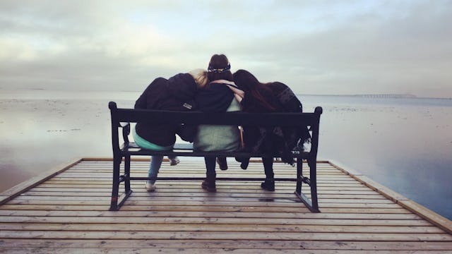 Three friends sitting on a bench in front of the sea and hugging each other