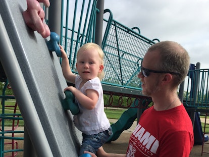 A father holding his toddler daughter on a rock-climbing wall at a playground