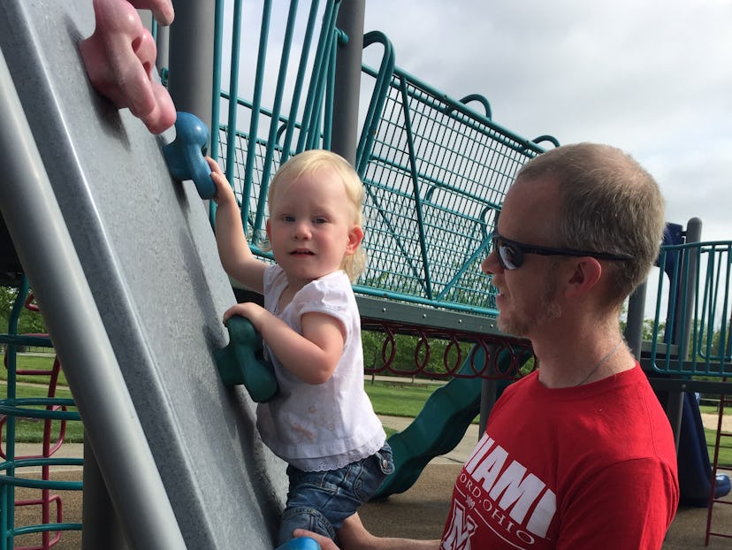 A father holding his toddler daughter on a rock-climbing wall at a playground