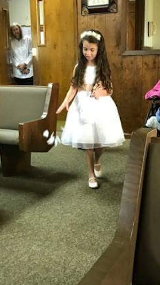 A girl wearing a white dress for her role of a flower girl at a wedding.