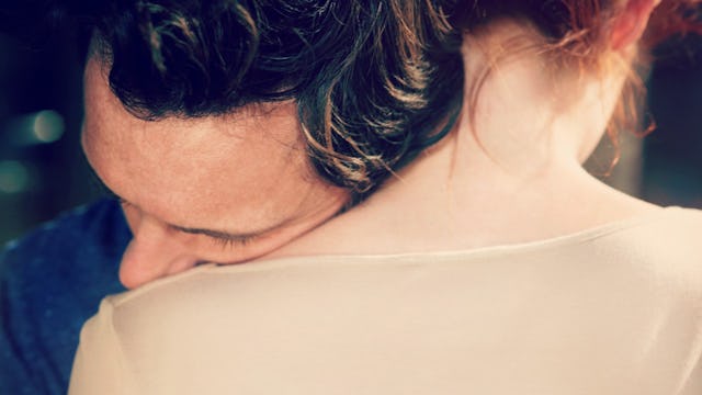 A brown-haired man in a blue shirt, leaning his head on the left shoulder of his wife in a beige T-s...