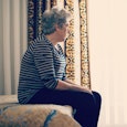 An elderly mom that has dementia sitting on the edge of a bed 