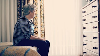 An elderly mom with dementia sitting on the edge of a bed 