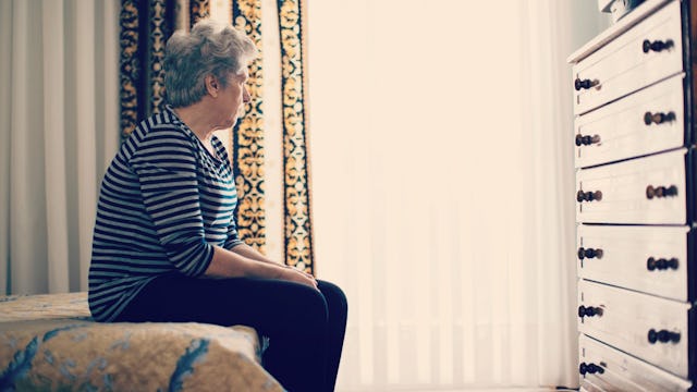 An elderly mom with dementia sitting on the edge of a bed