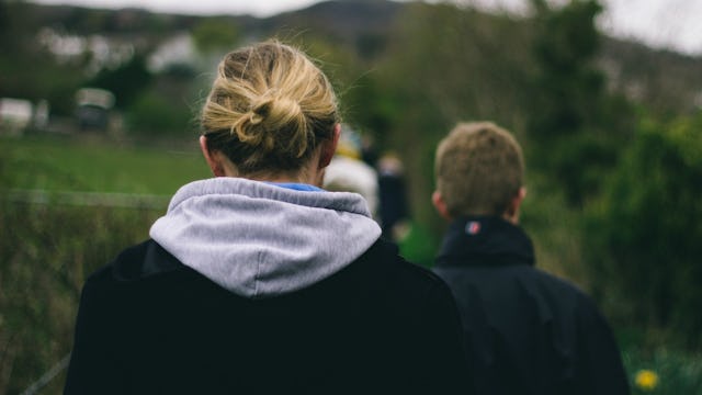 A woman in a black jacket walking behind a male person