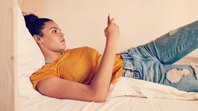 Girl in college laying on her bed with her phone looking lonely