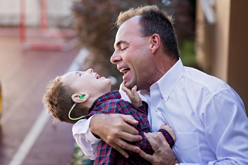 A father holding his child while both of them are smiling during a sunny day