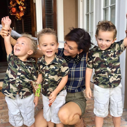 A happy mother with short brown hair next to her three boys who are dressed in camo print t-shirts