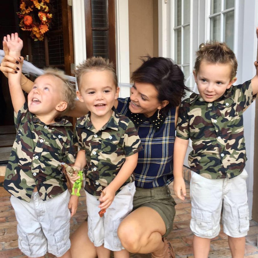 A happy mother with short brown hair next to her three boys who are dressed in camo print t-shirts
