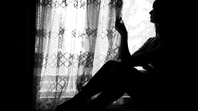 A woman with a chronic illness sitting next to a window in black and white