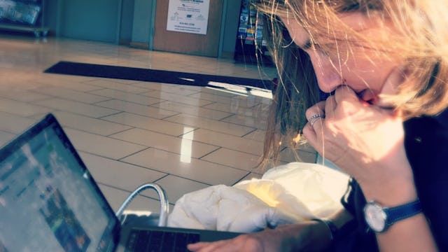 A woman sitting in the hallway, working on her laptop who is her kids' personal assistant