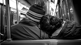Black and white picture of a couple leaning their heads against each other while sitting in the publ...