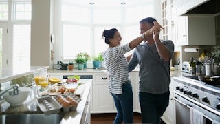 Wife dancing with her older husband in the kitchen while making breakfast 