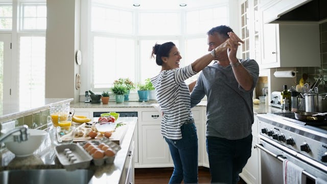 Wife dancing with her older husband in the kitchen while making breakfast