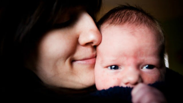 A close-up of a new mother smiling and holding her baby next to her face