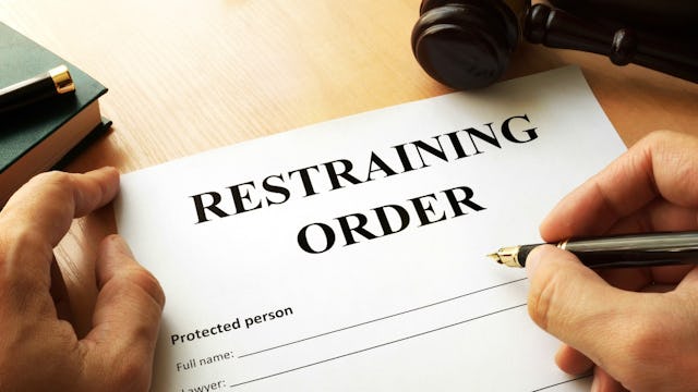 A restraining order document and a hand holding a pen, ready to sign