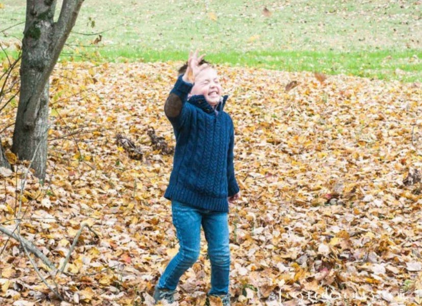 Misty Nelson's son smiling and playing with fallen leaves in a park