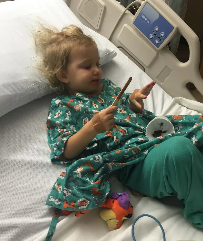A child lying in a hospital bed in green pajamas playing with toys