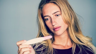 A woman holding a pregnancy test and looking disappointed due to infertility problems