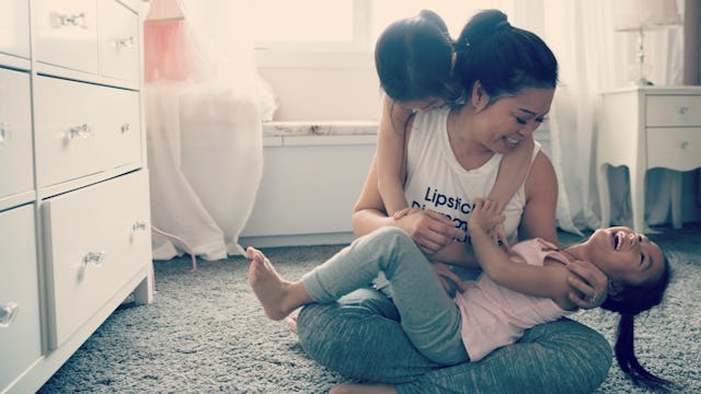 A woman playing with two of her daughters and tickling one of them.