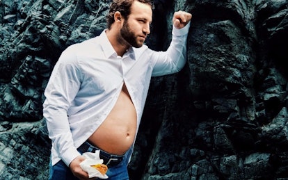 A new dad wearing a white half-buttoned shirt with his belly sticking out holding a small burger whi...