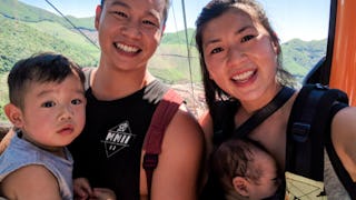 Tina Pik holding her newborn while standing next to her husband who's holding their toddler, smiling...