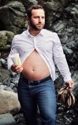 A new dad wearing a white half-buttoned shirt with his belly sticking out holding a drink in his han...