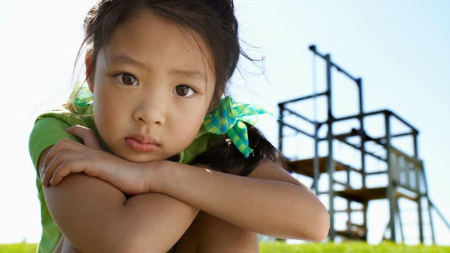 Little Girl Squatting Down With Her Arms Crossed On Her Knees And Looking Straight Ahead
